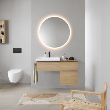 Łazienka z szarymi ścianami, drewnianymi meblami łazienkowymi Geberit i okrągłym podświetlanym lustrem Geberit Option