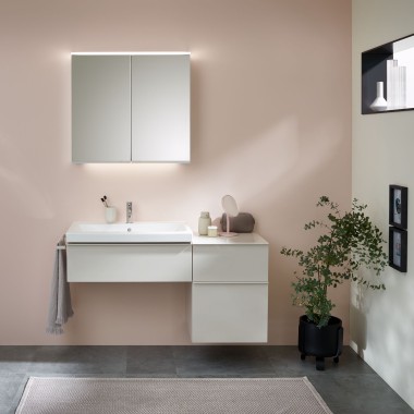 Przestrzeń umywalkowa z meblami łazienkowymi, umywalką i szafką z lustrem firmy Geberit przed pastelową ścianą