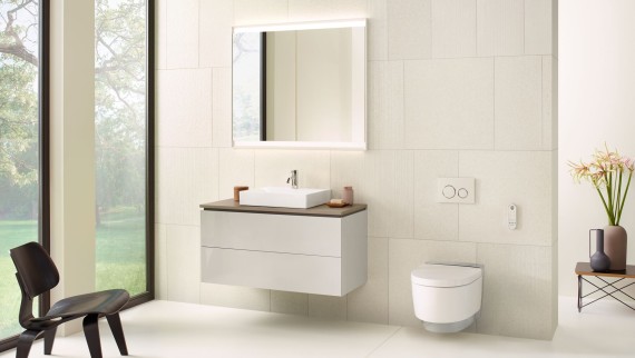 Biała łazienka z szafką z lustrem, szafką pod umywalkę, przyciskiem uruchamiającym i ceramiką sanitarną firmy Geberit