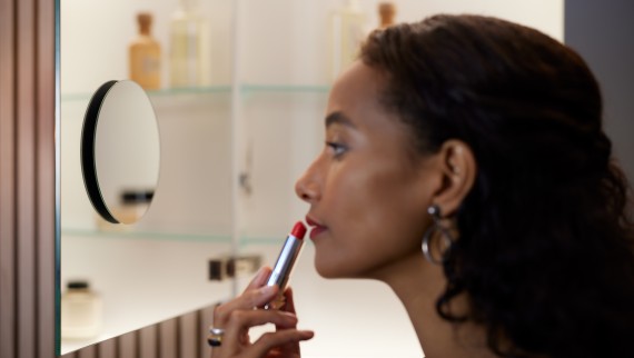 Kobieta nakładająca szminkę na usta przed lustrem powiększającym (© Geberit)